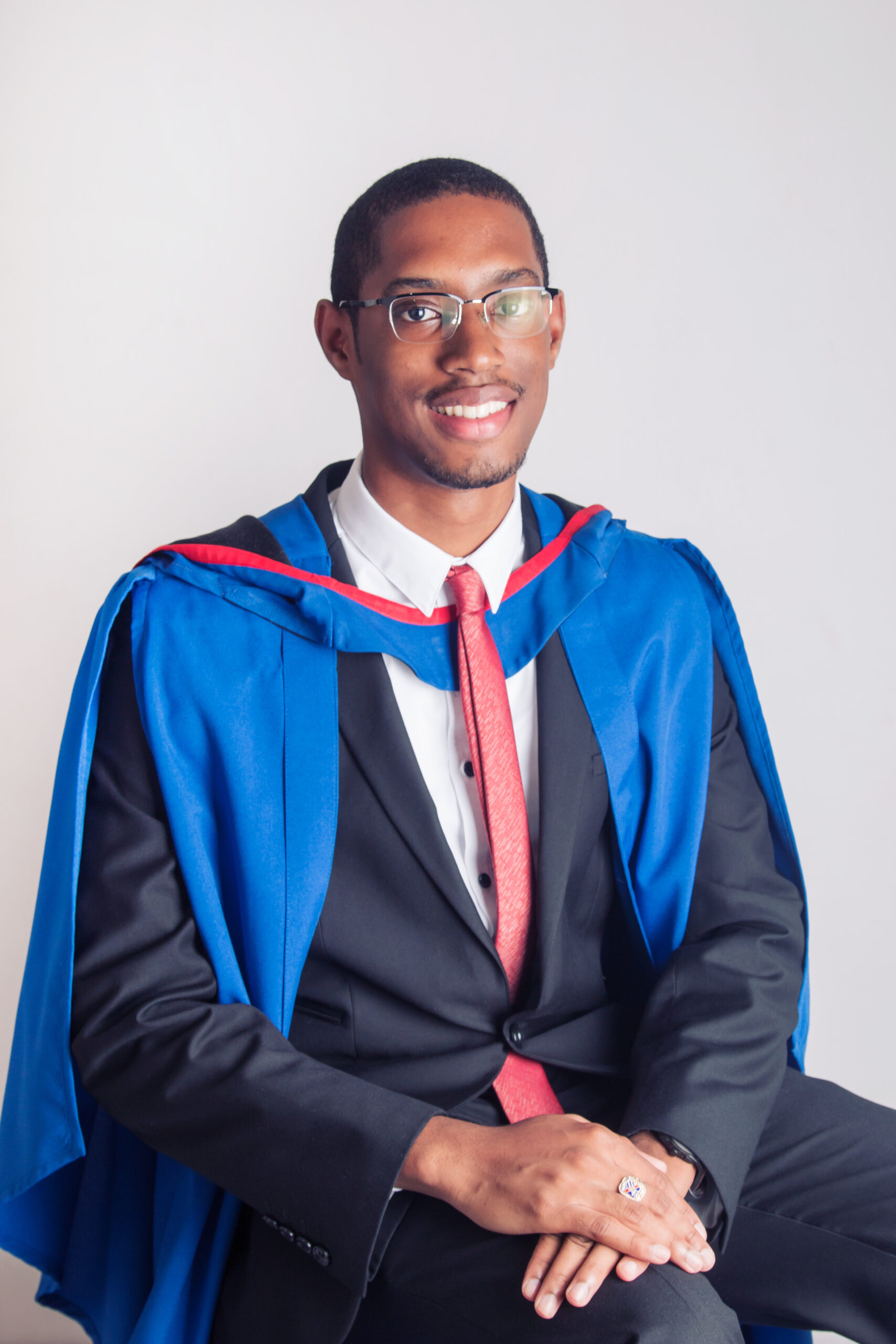 Seated graduate in a blue and red gown at Define Studios