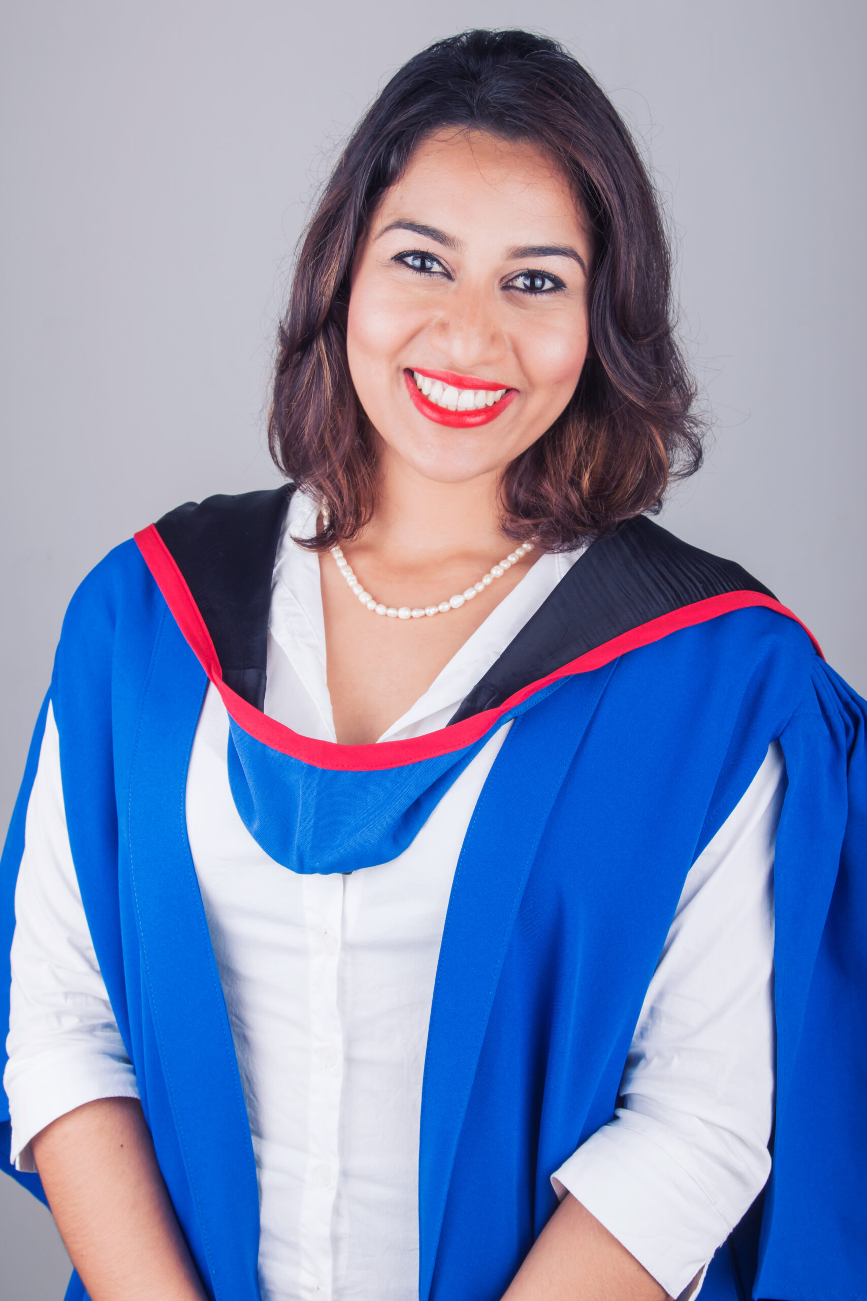Smiling graduate wearing a blue and red gown in the Define Studios portrait studio