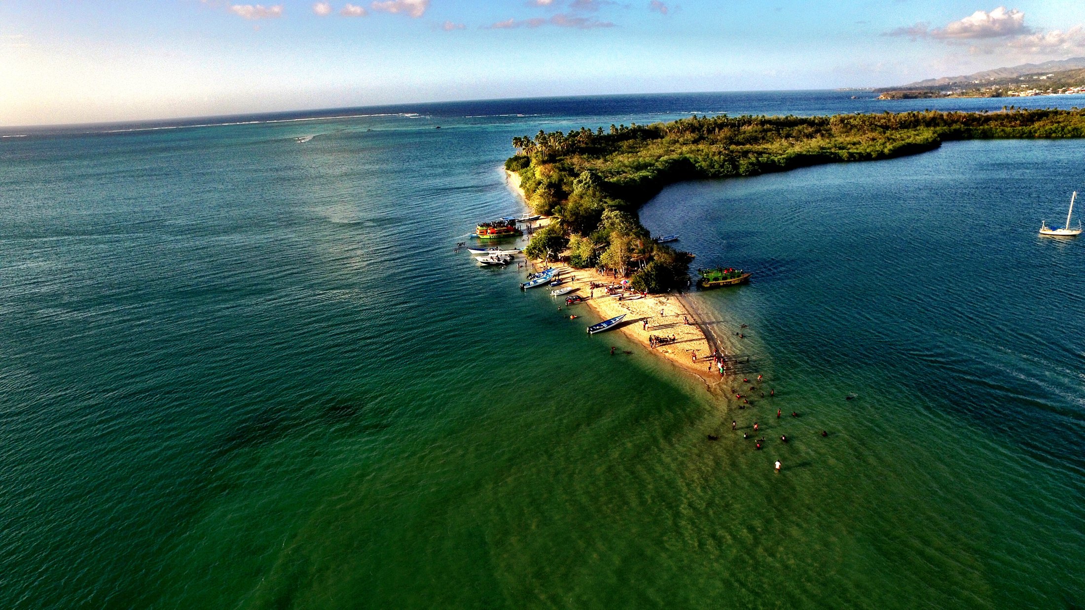 No Man's Land, Tobago: A narrow sandy, tree-covered point divides shallow green water, with small boats and people along the shore.